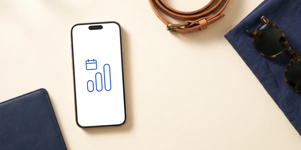 A phone showing three rounded bars of rising height under a calendar icon, beside a navy passport, a coiled tan leather strap, a folded navy linen cloth and sunglasses